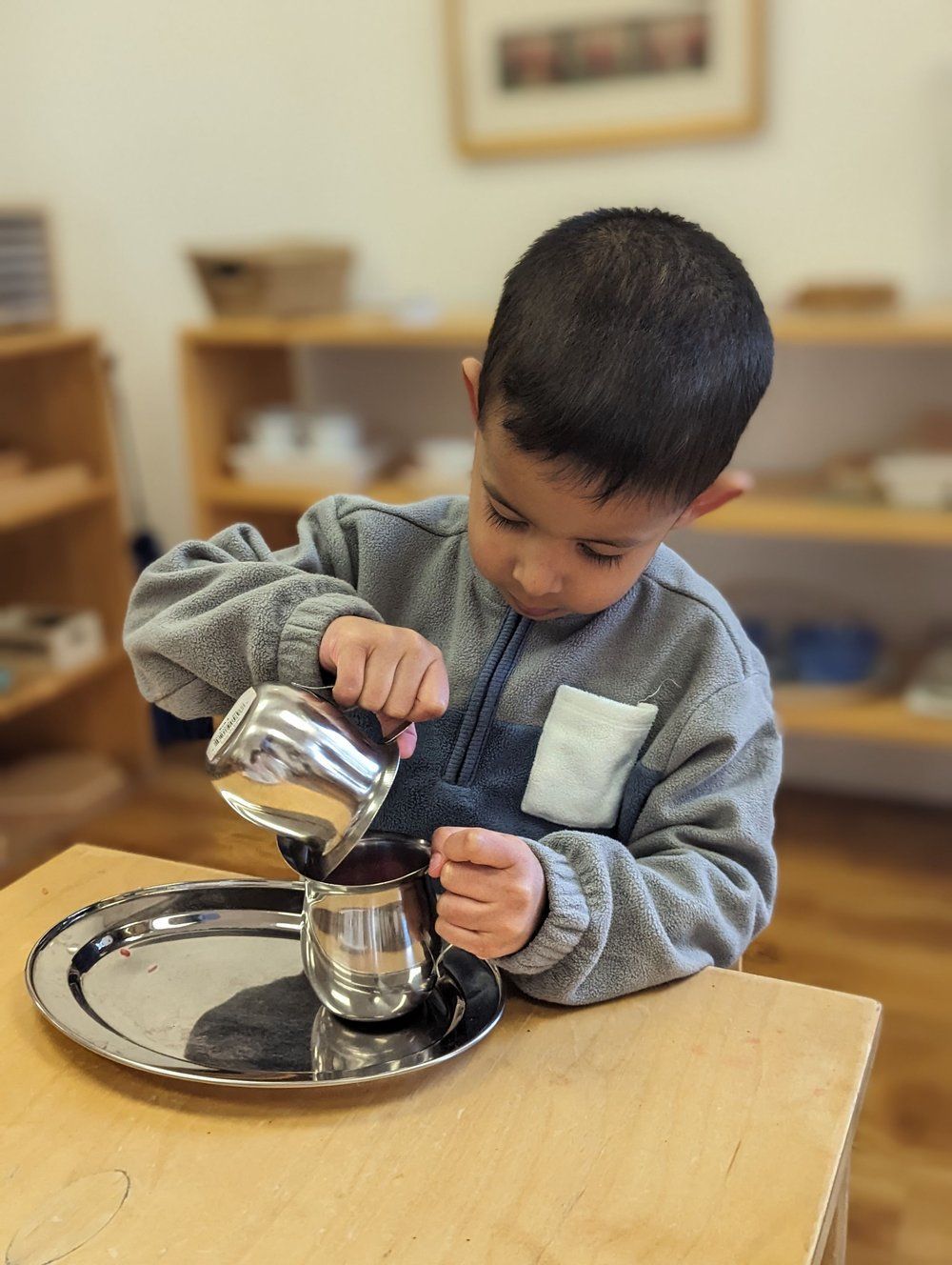 A young boy is pouring water into a cup on a tray.