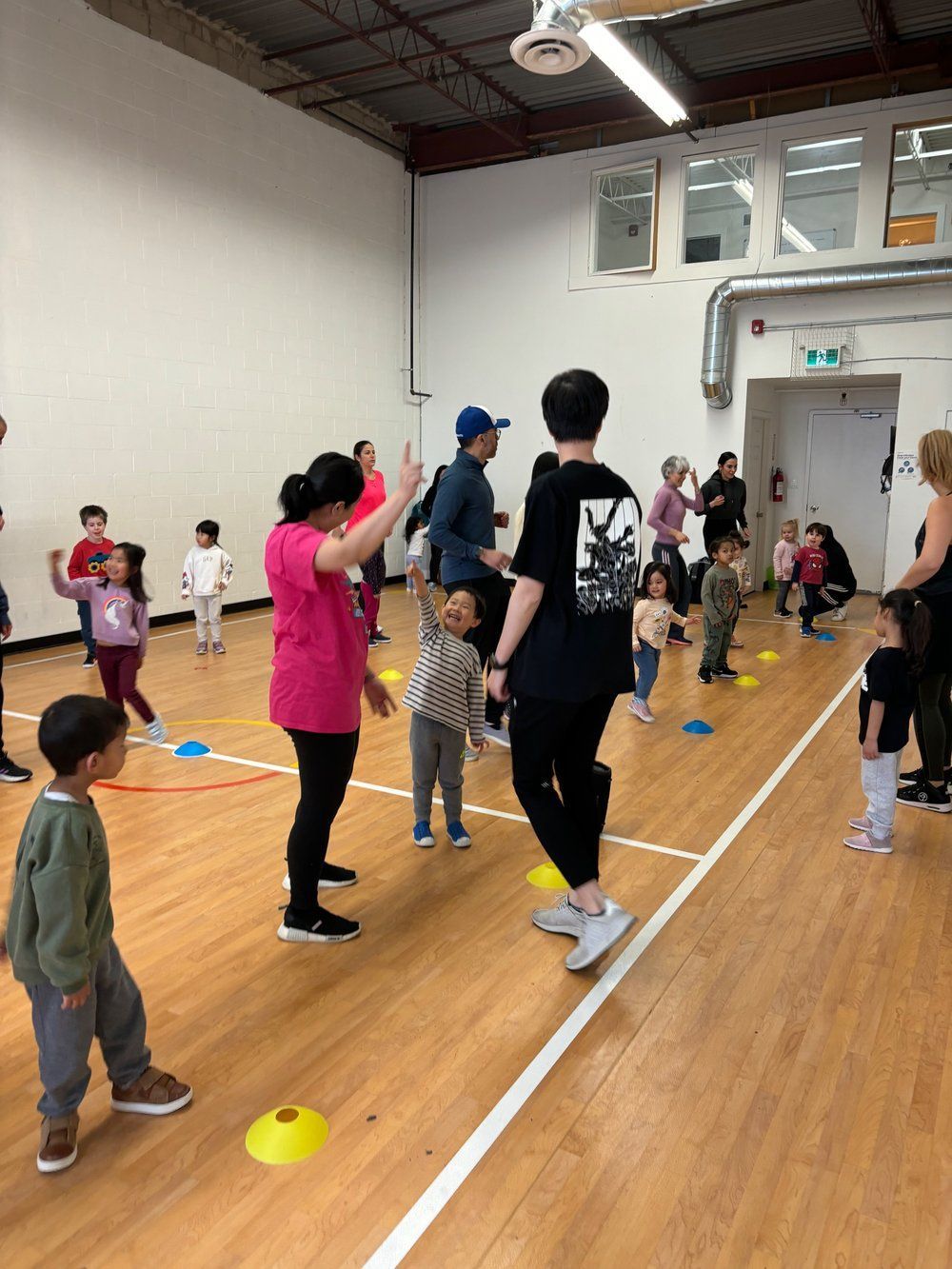 A group of people are standing on a wooden floor in a gym.