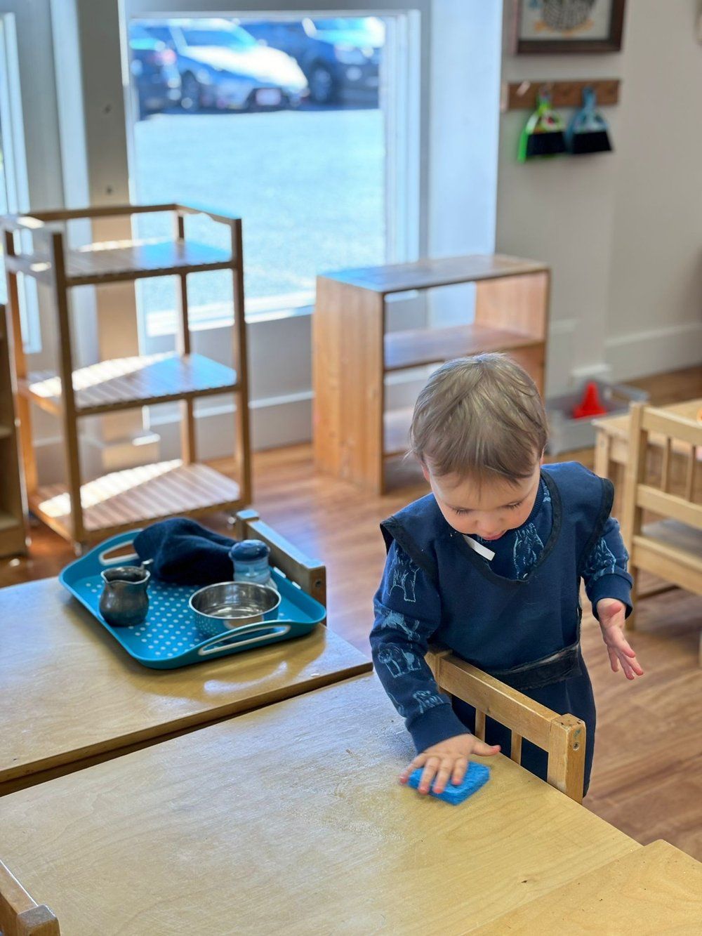 A young boy is playing with a blue toy on a wooden table.