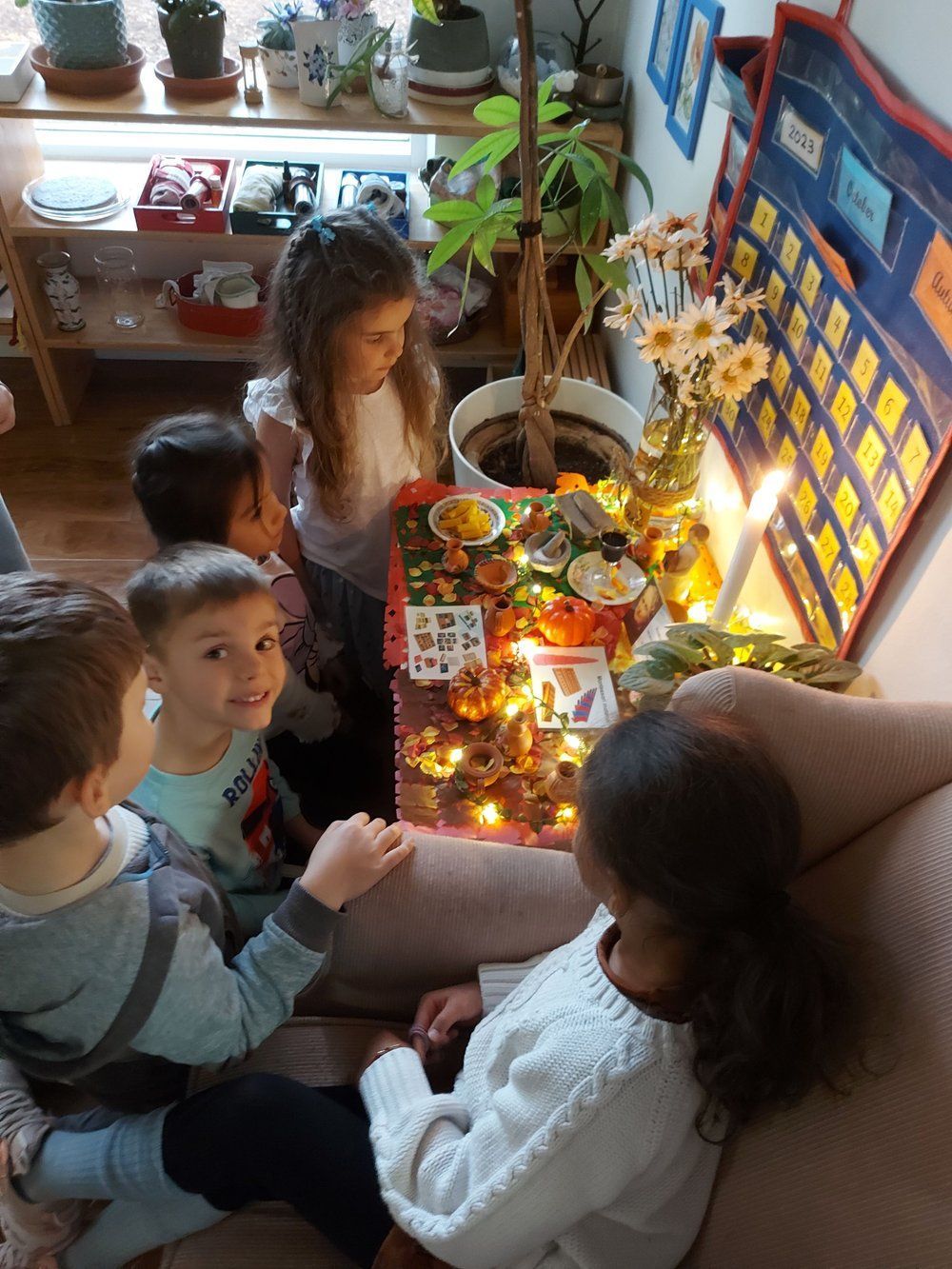 A group of children are sitting around a table with a candle on it.