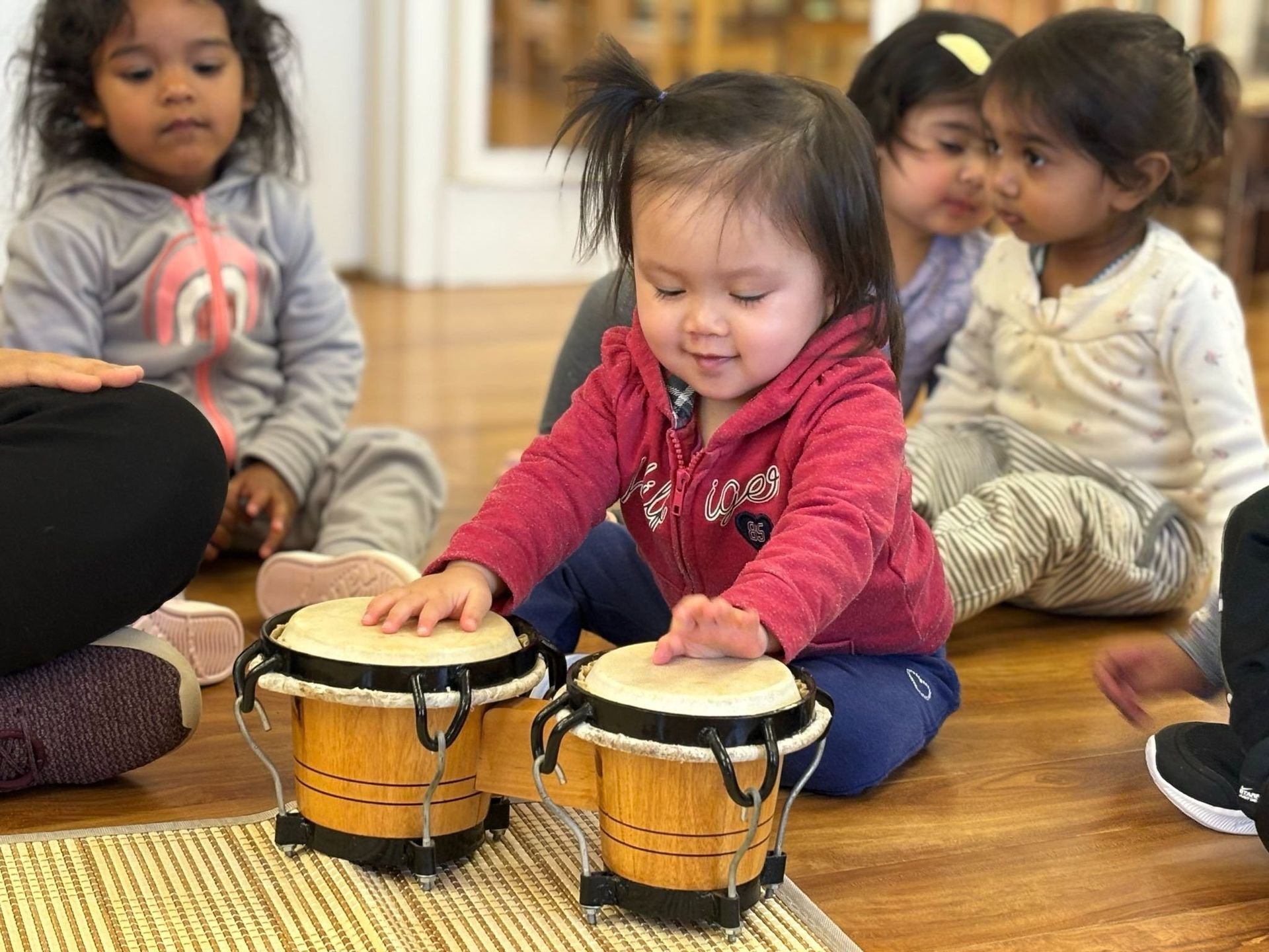 A group of young girls are sitting on the floor playing drums.