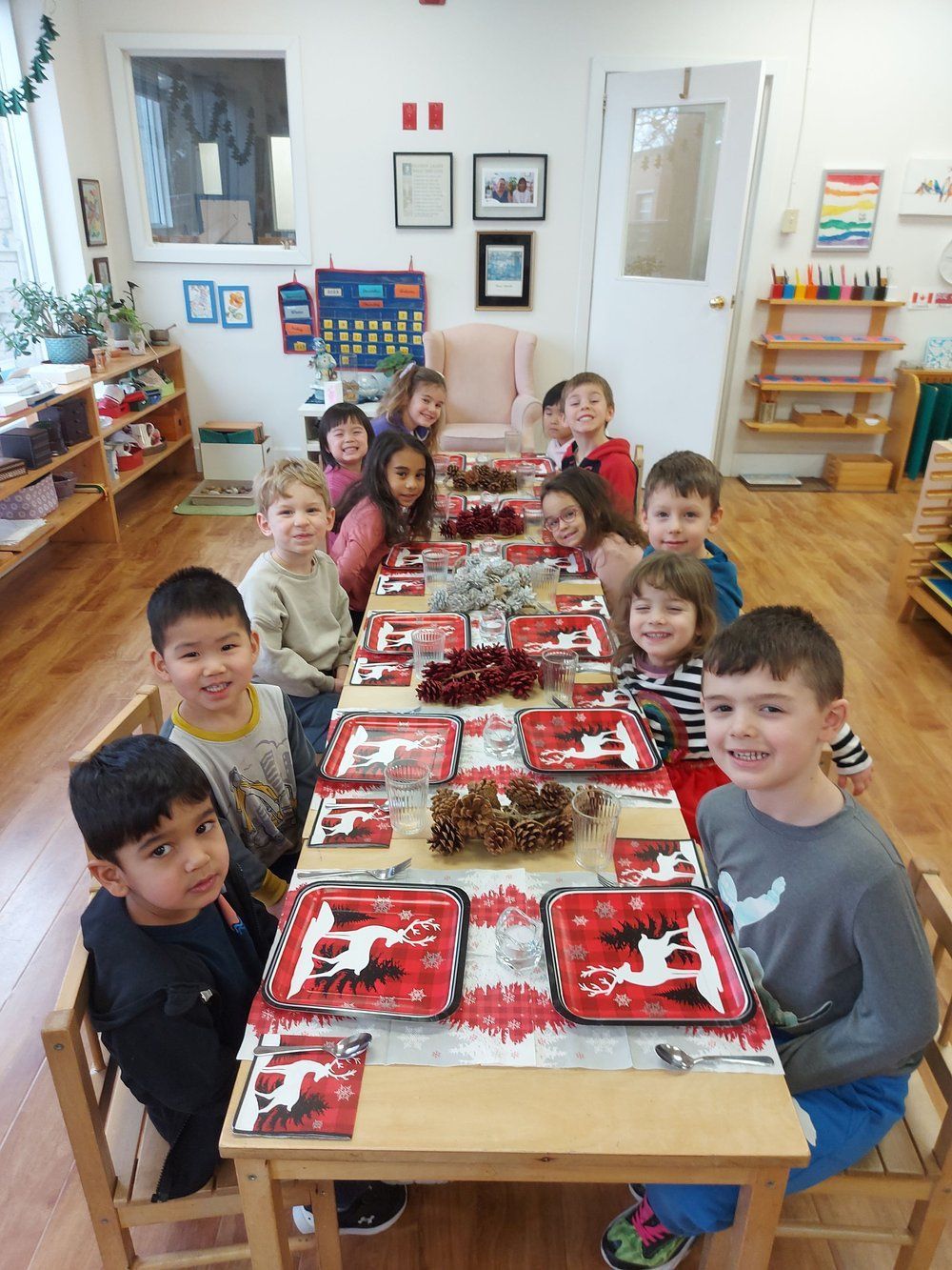 A group of children are sitting at a long table in a classroom.