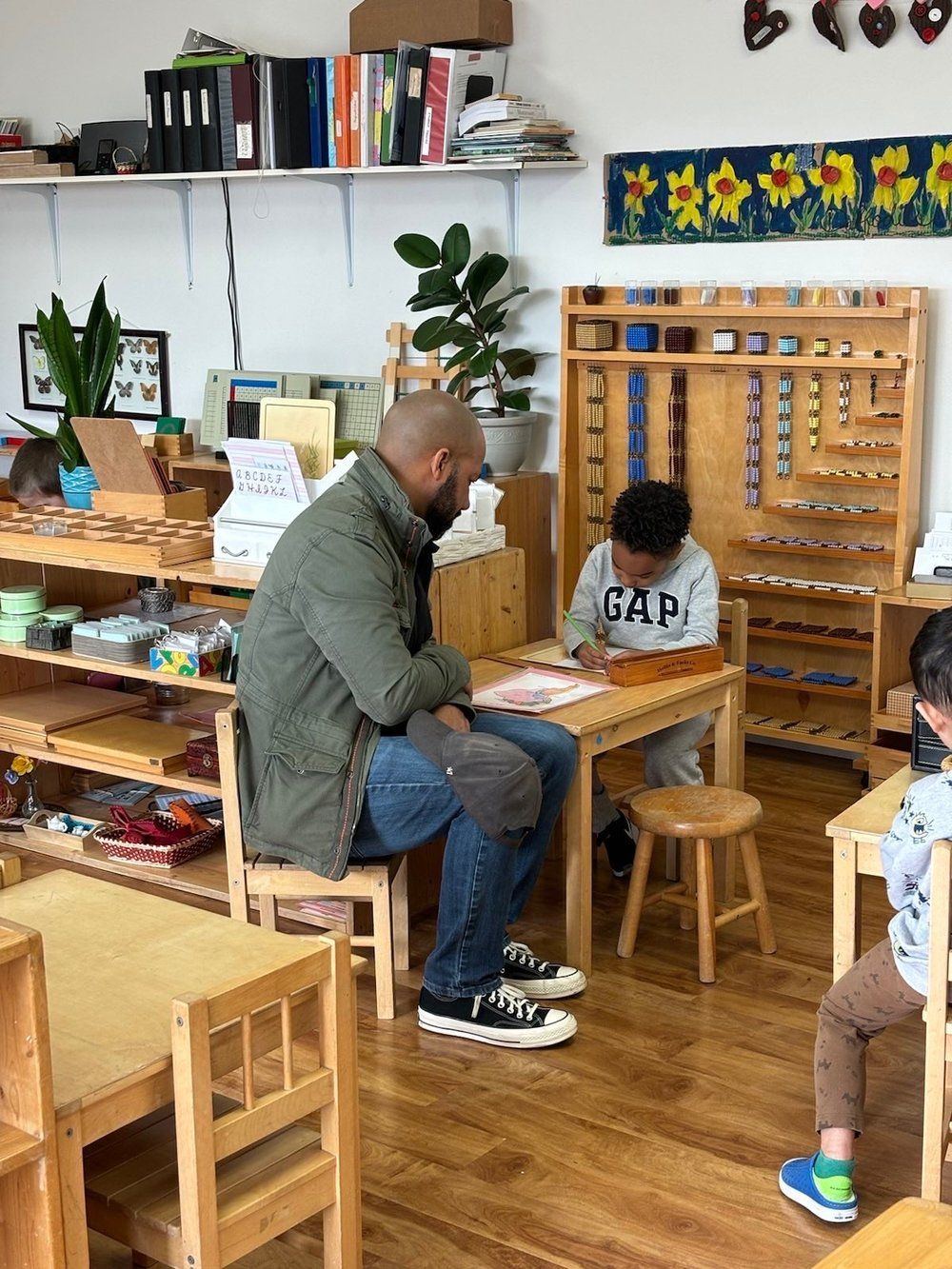 A man is sitting at a table with a child in a classroom.