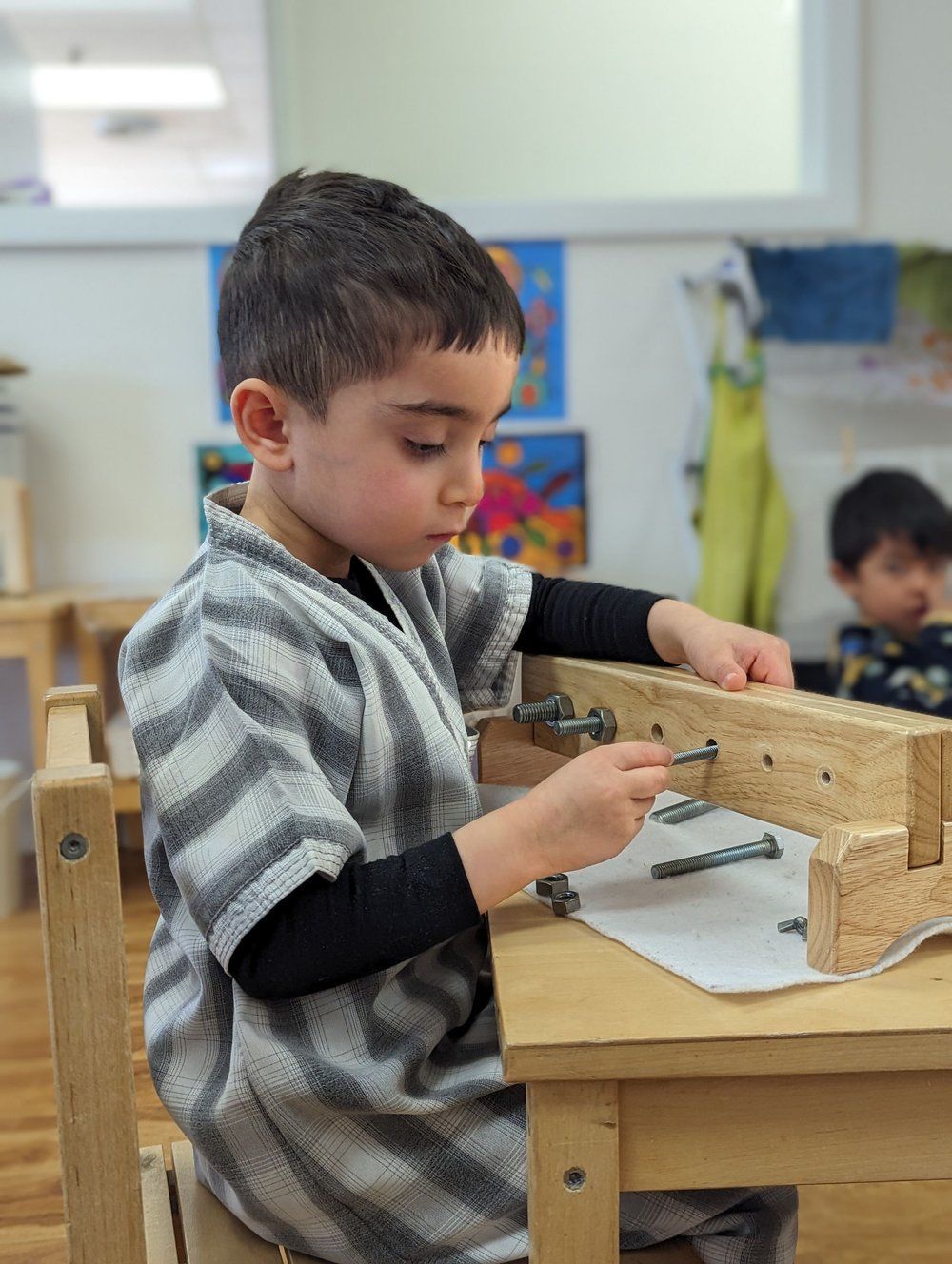A young boy is sitting at a wooden table playing with nails.