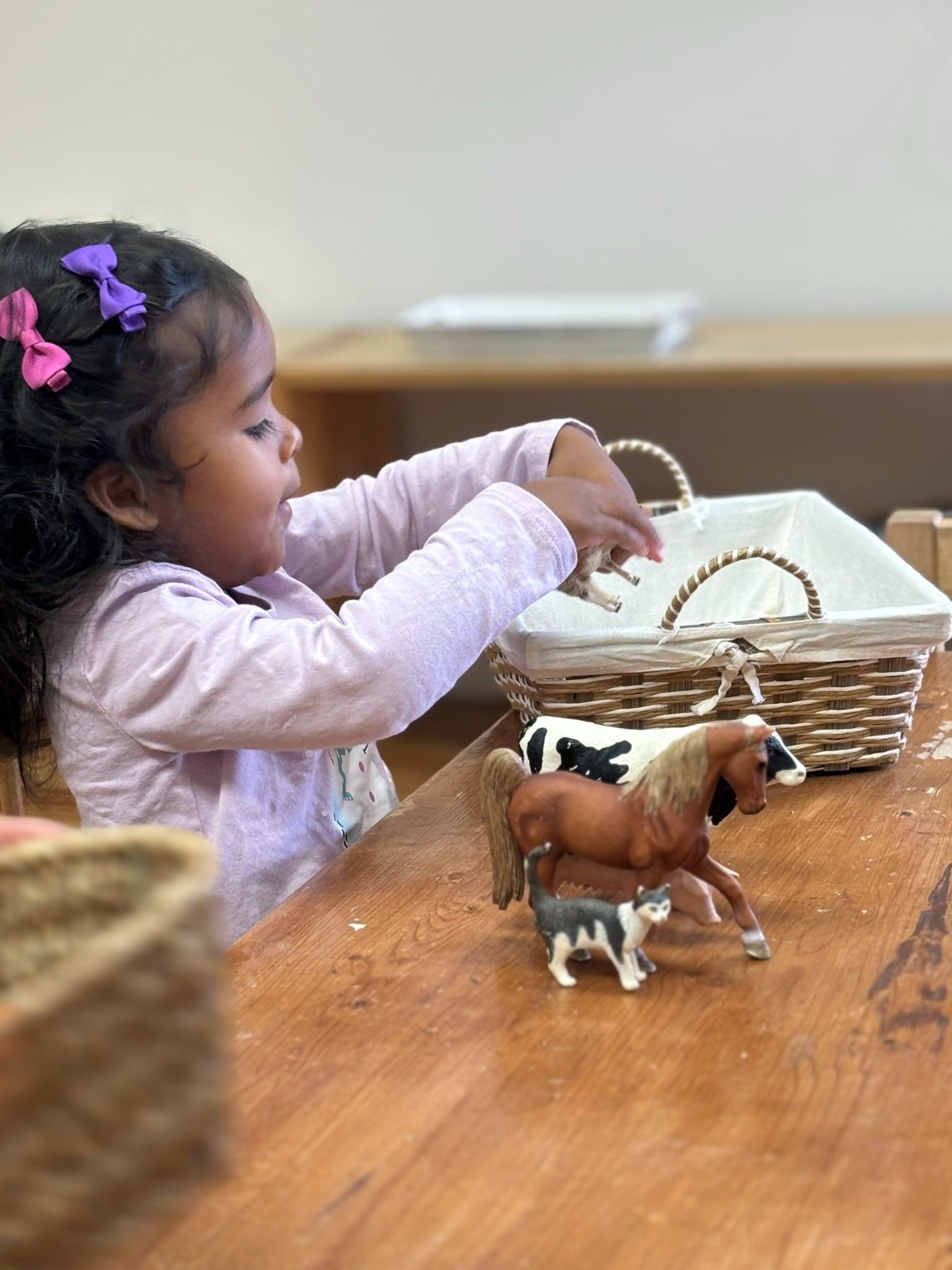 A little girl is sitting at a table playing with toy horses.