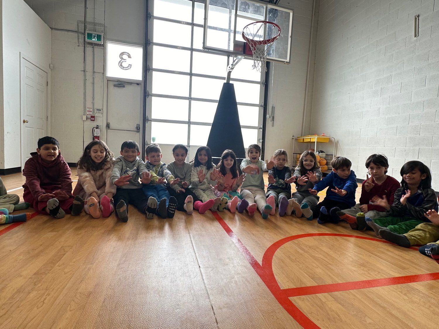 A group of children are sitting on the floor of a basketball court.