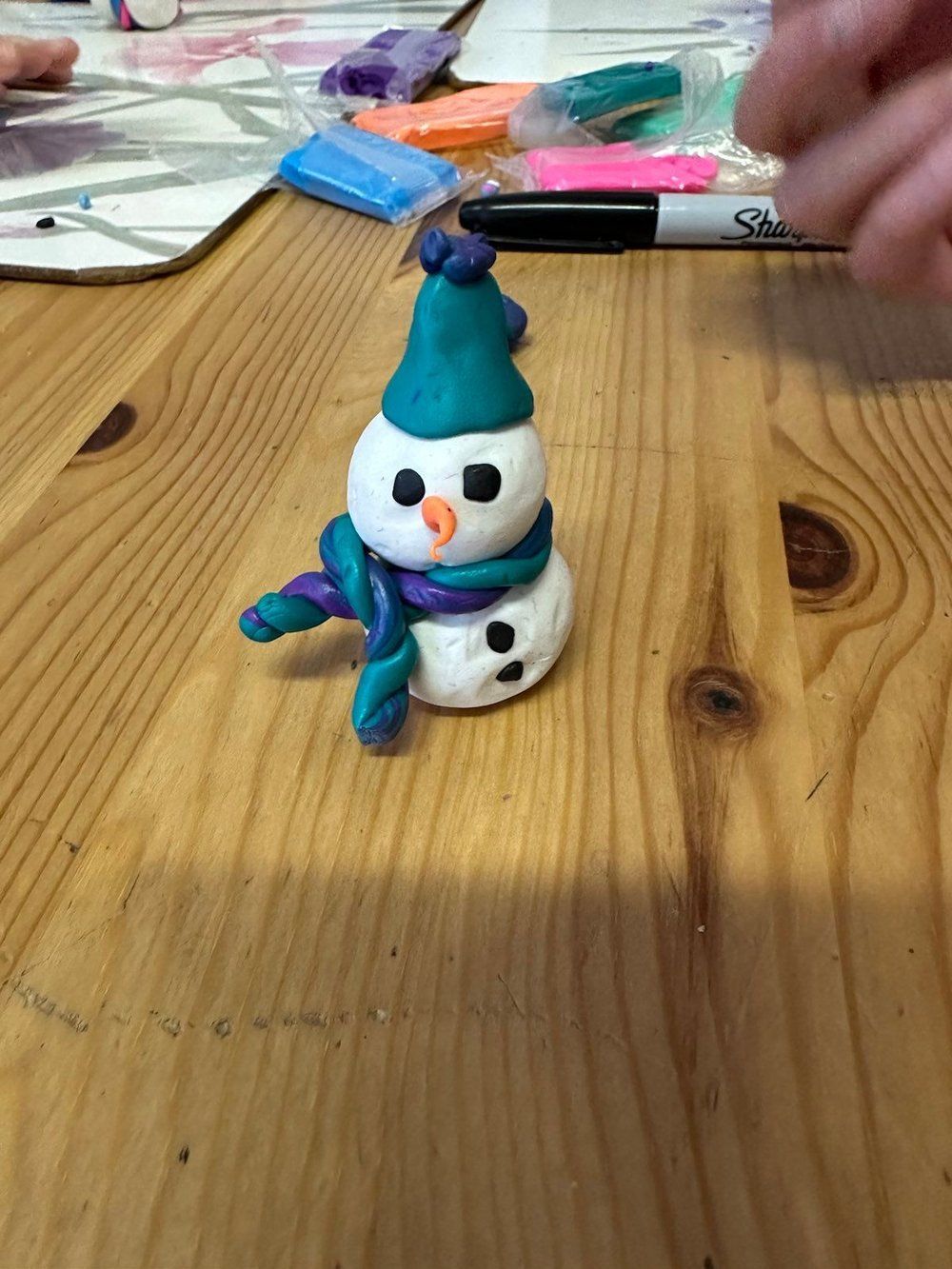 A snowman made out of play dough is sitting on a wooden table.