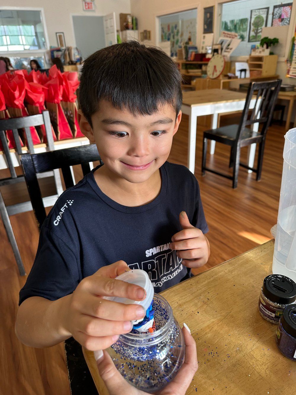 A young boy is sitting at a table holding a plastic bottle.