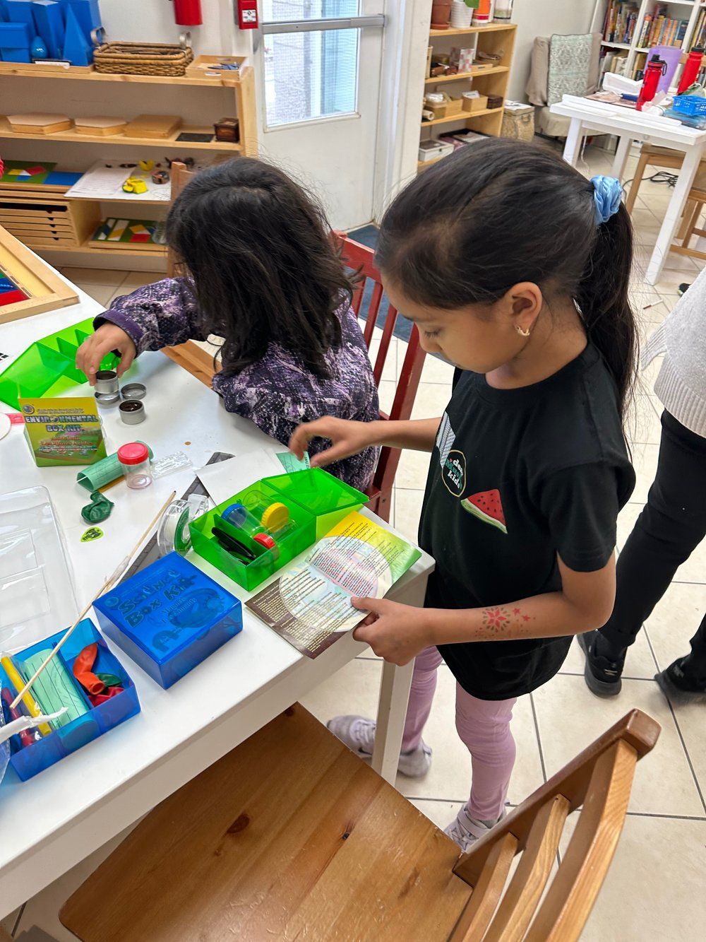 Two young girls are playing with clay at a table in a classroom.
