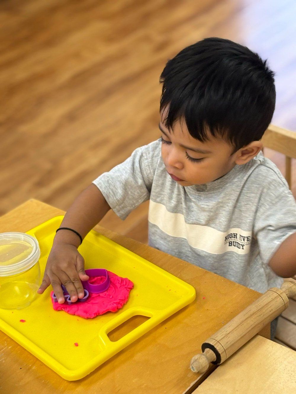 A young boy is playing with play dough on a yellow cutting board.