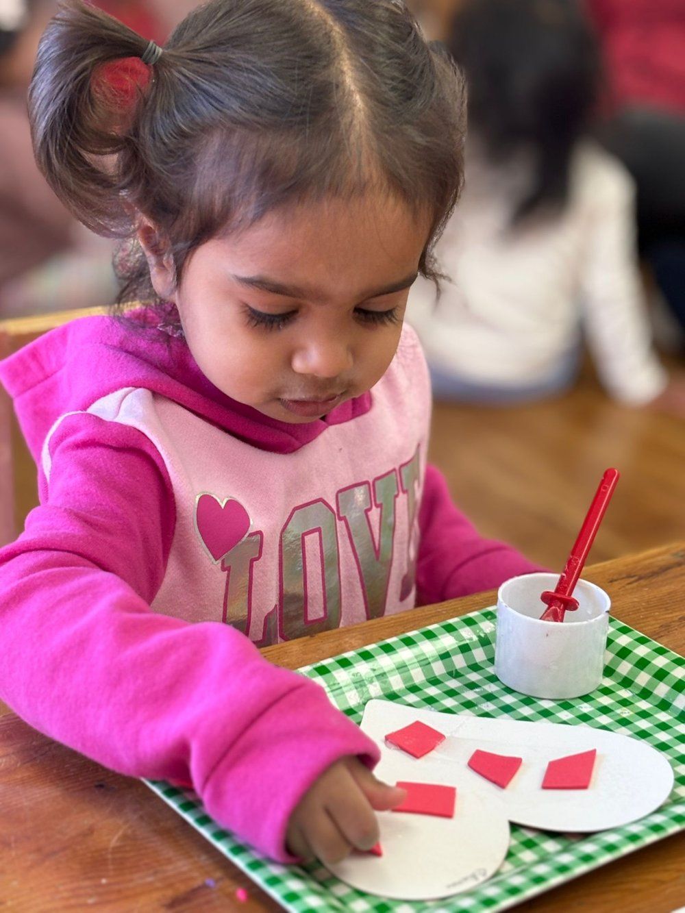 A little girl in a pink shirt with the word love on it is sitting at a table.