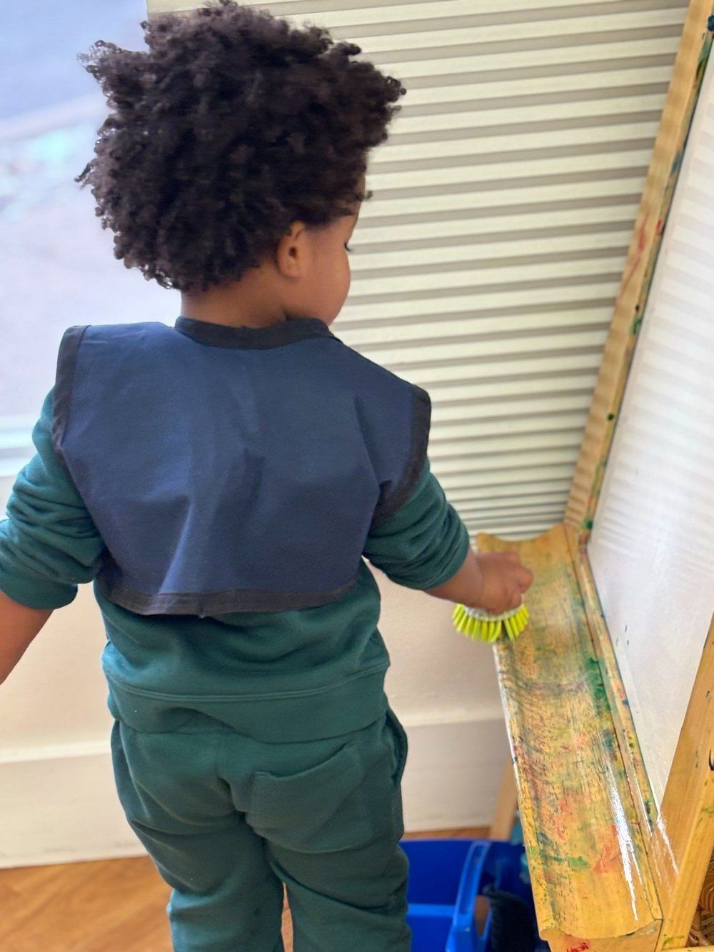 A young boy is standing in front of a wooden easel.