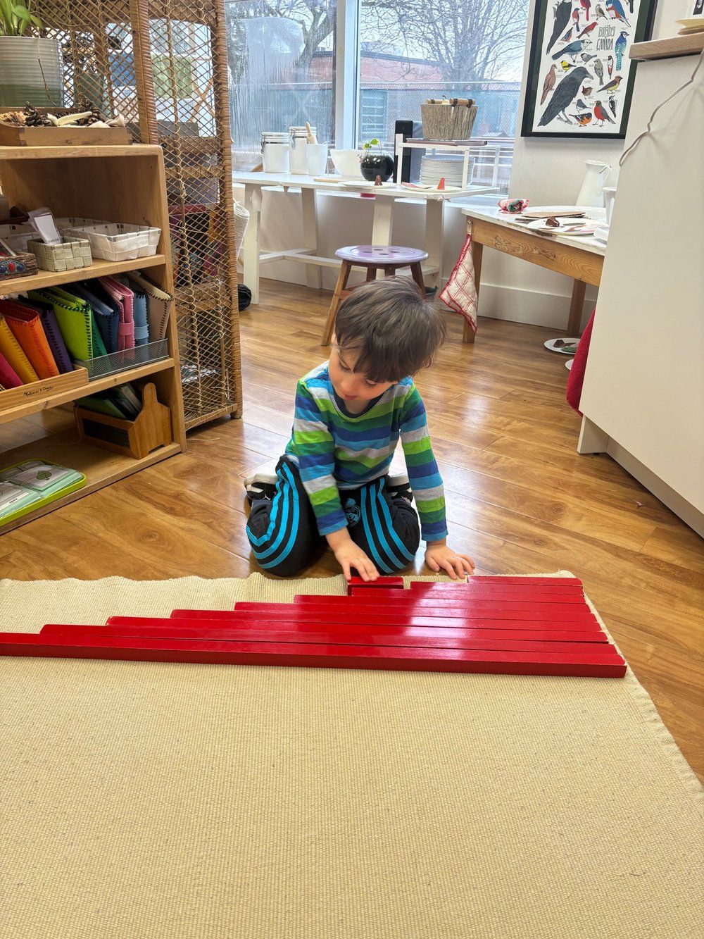 A young boy is sitting on the floor playing with red blocks.