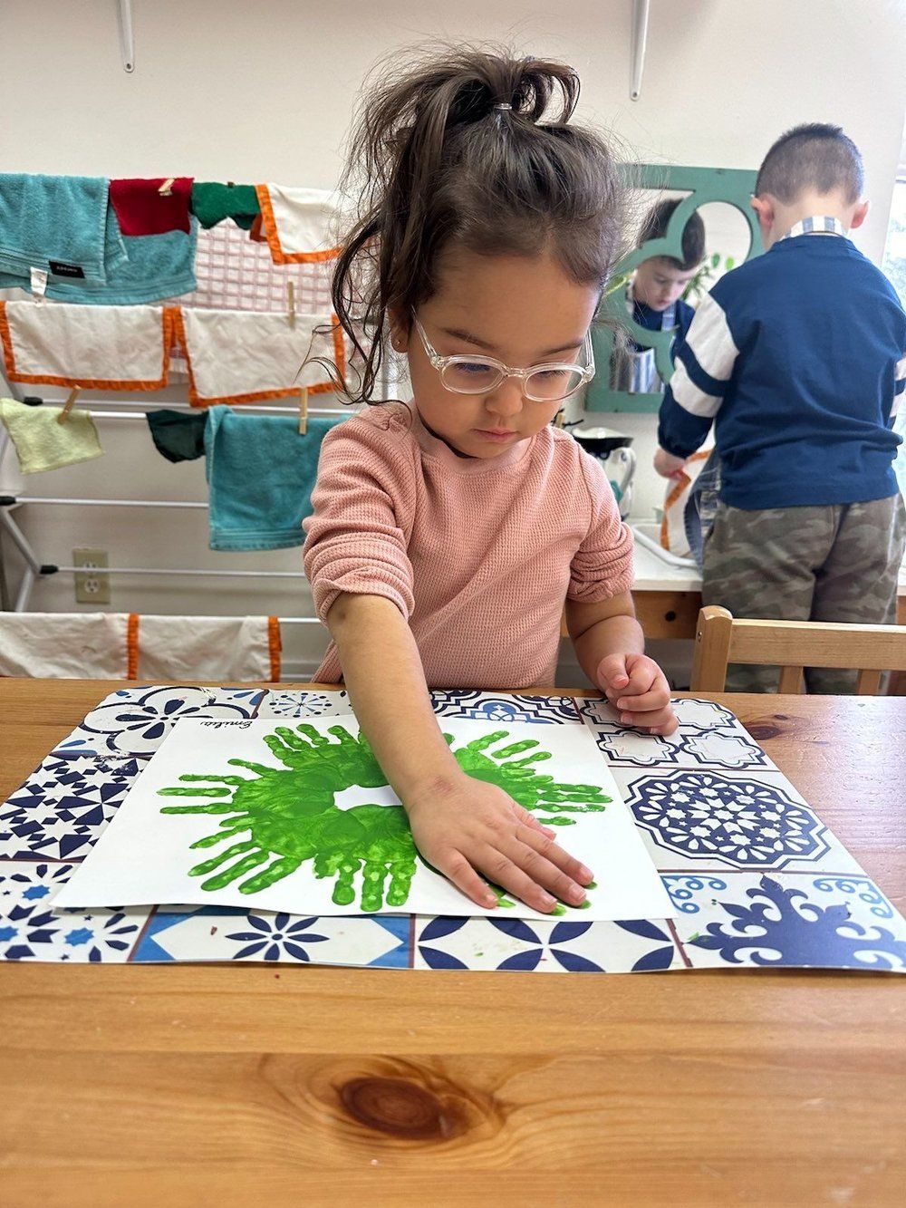 A little girl is sitting at a table painting with her hands.