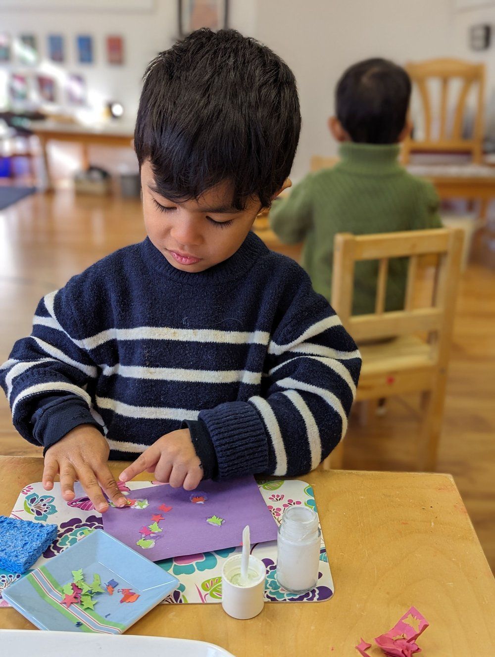 A young boy is sitting at a table playing with stickers