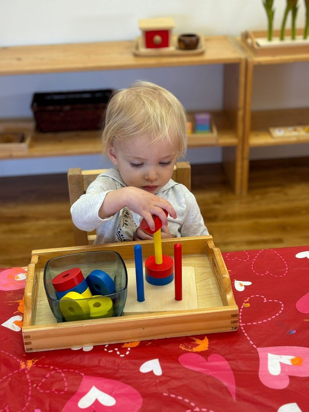 A little girl is playing with a wooden toy on a table.