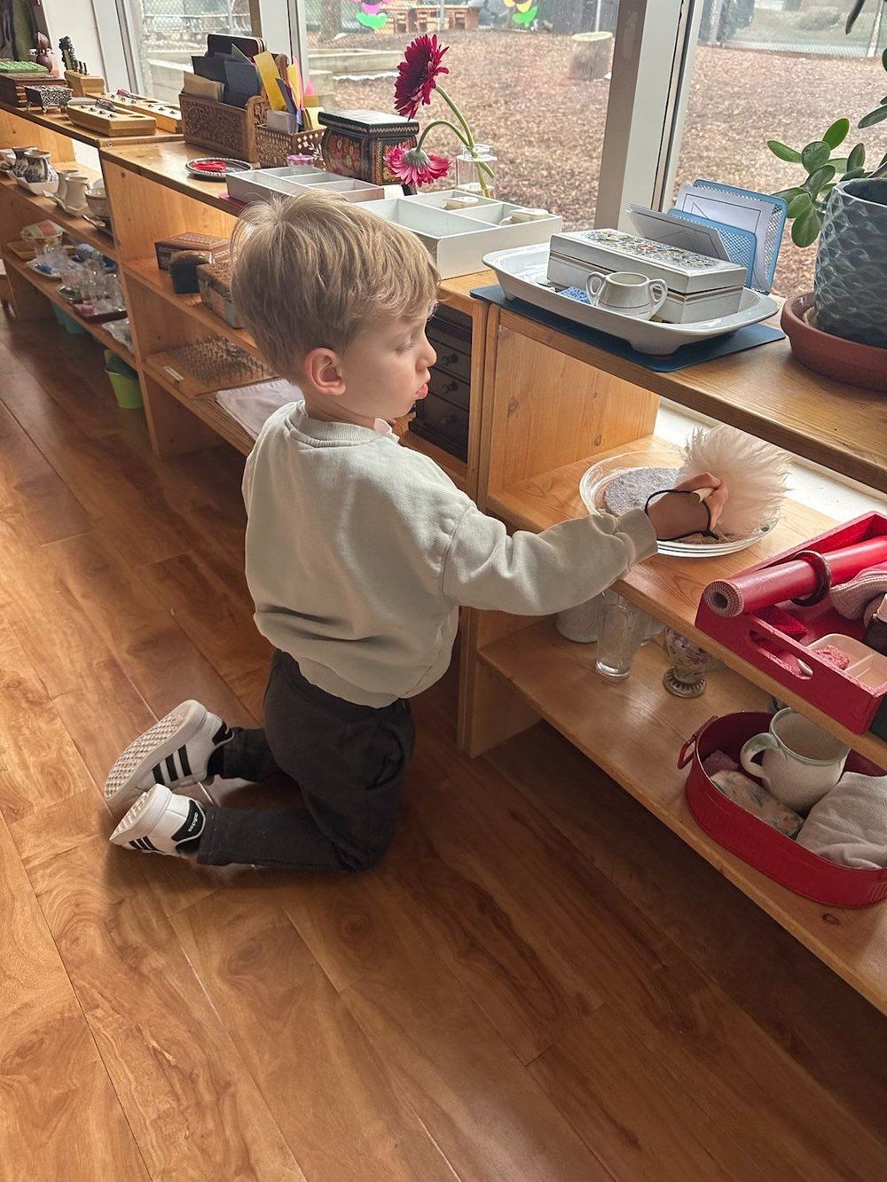 A young boy is kneeling down in front of a wooden shelf.