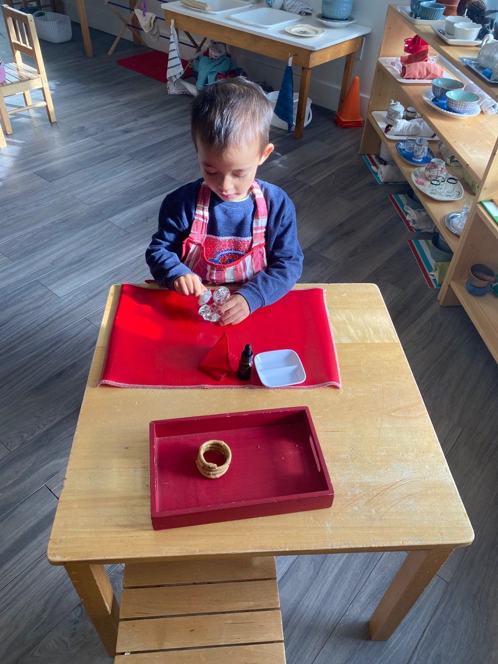 A young boy is sitting at a wooden table playing with a red tray.