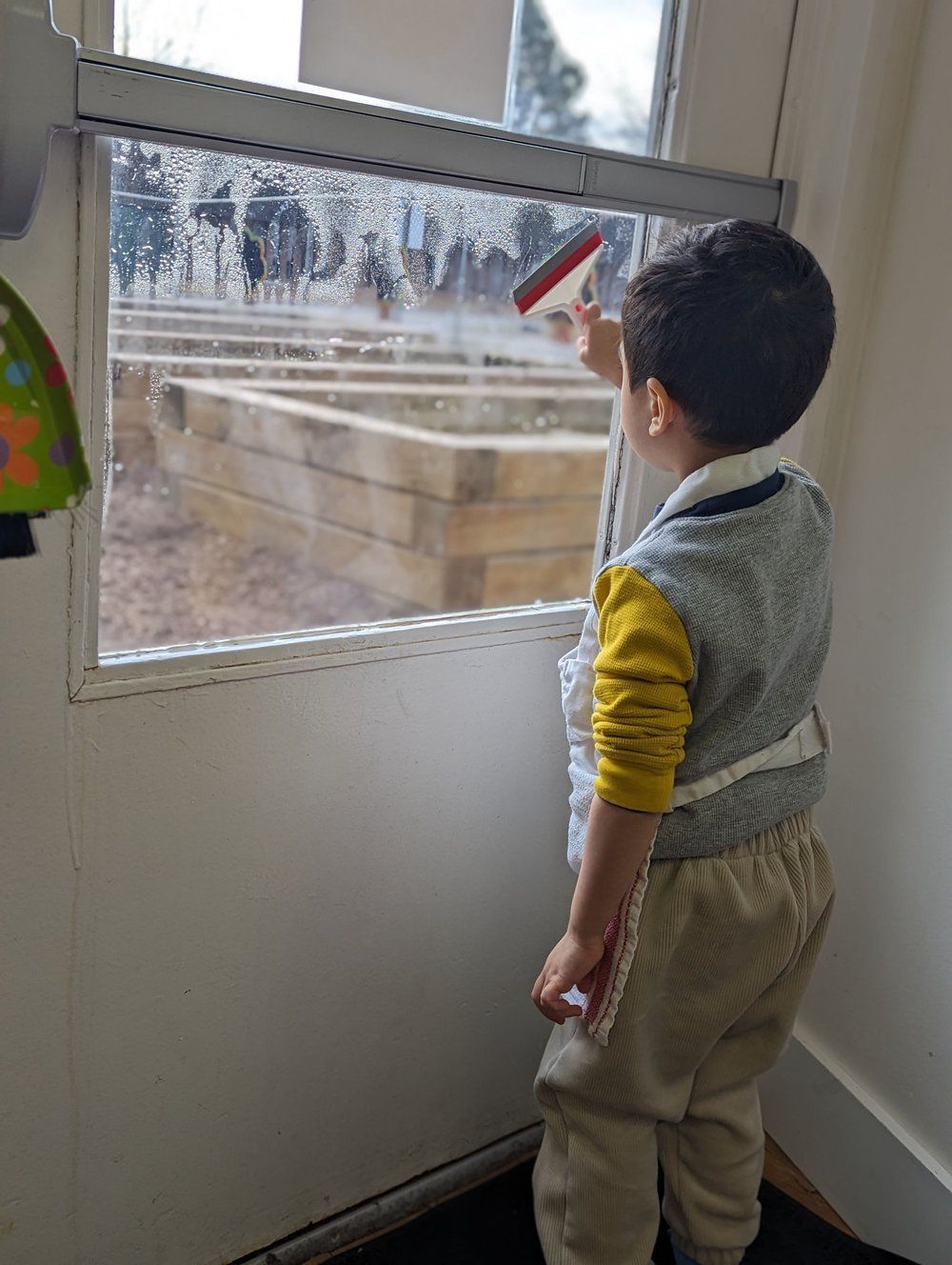 A young boy is cleaning a window with a brush.