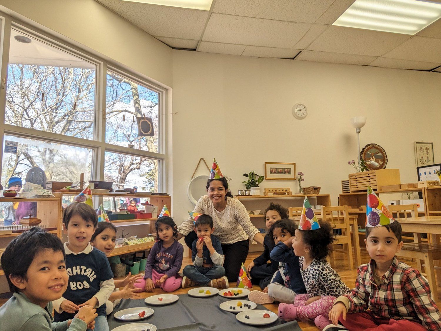A group of children are sitting around a table with plates of food.