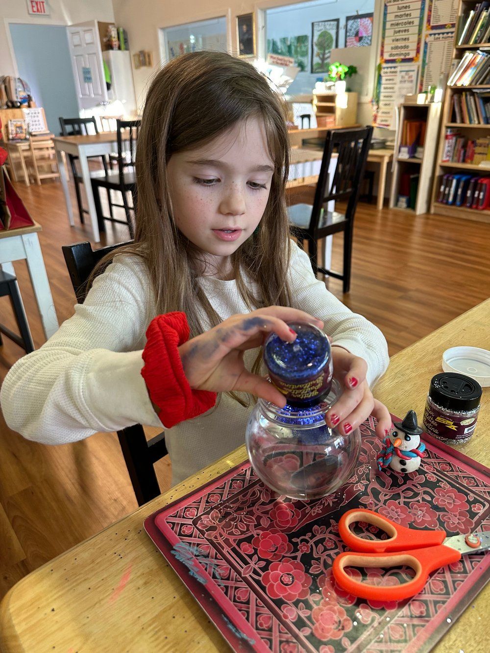 A little girl is sitting at a table making a craft.