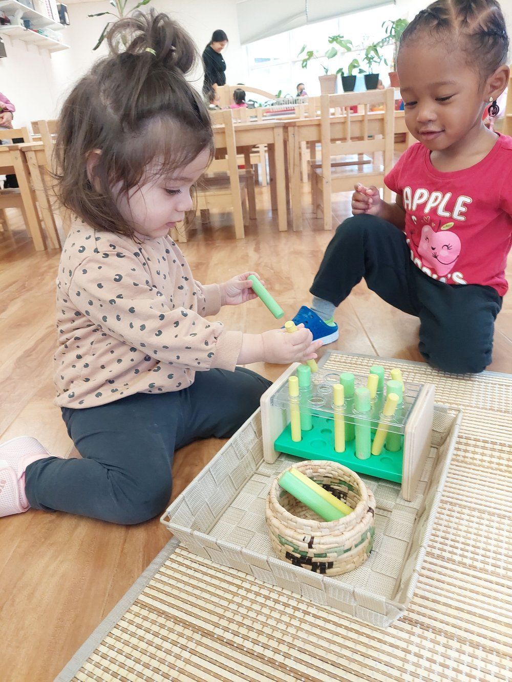 Two little girls are sitting on the floor playing with toys.