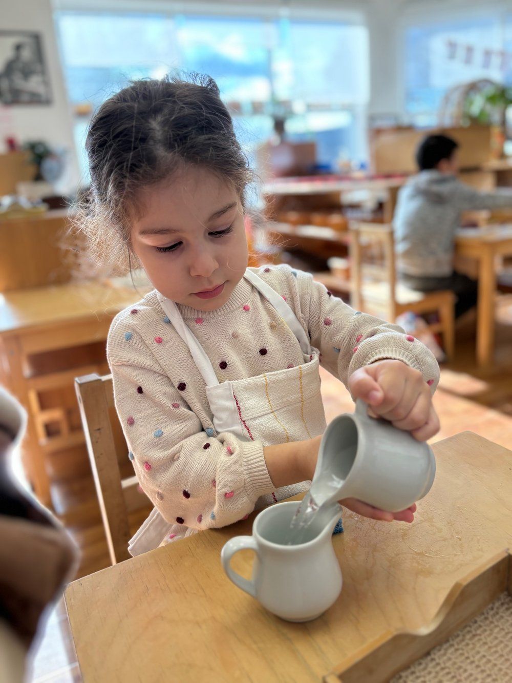 A little girl is pouring milk into a cup.