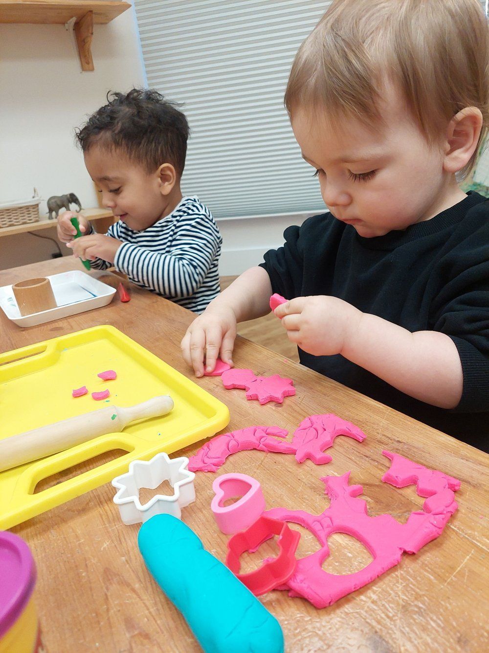 Two young children are playing with play dough on a wooden table.
