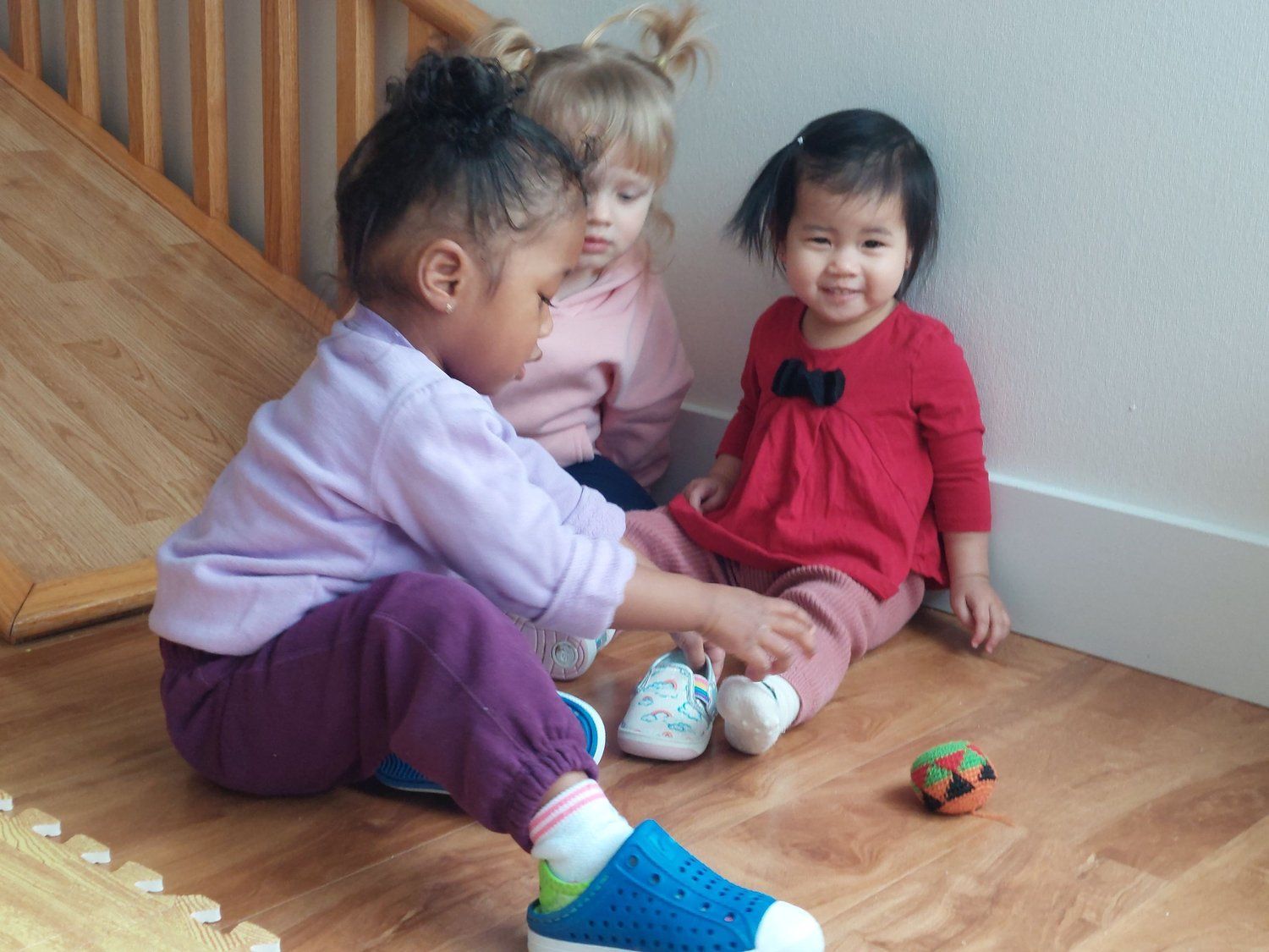 Three little girls are sitting on the floor playing with toys.