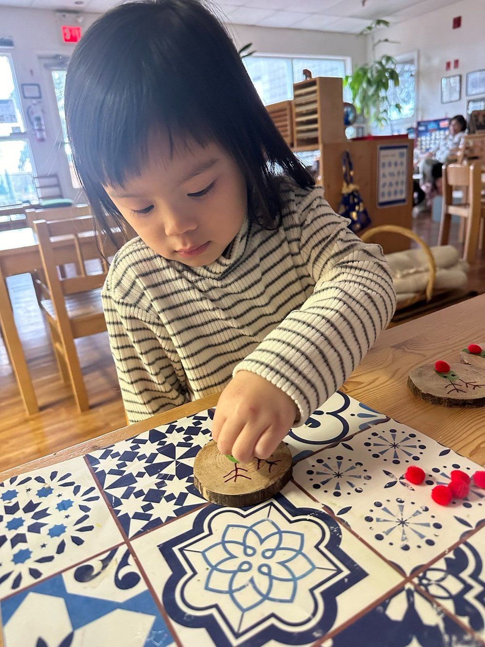 A little girl is sitting at a table playing with a piece of wood.