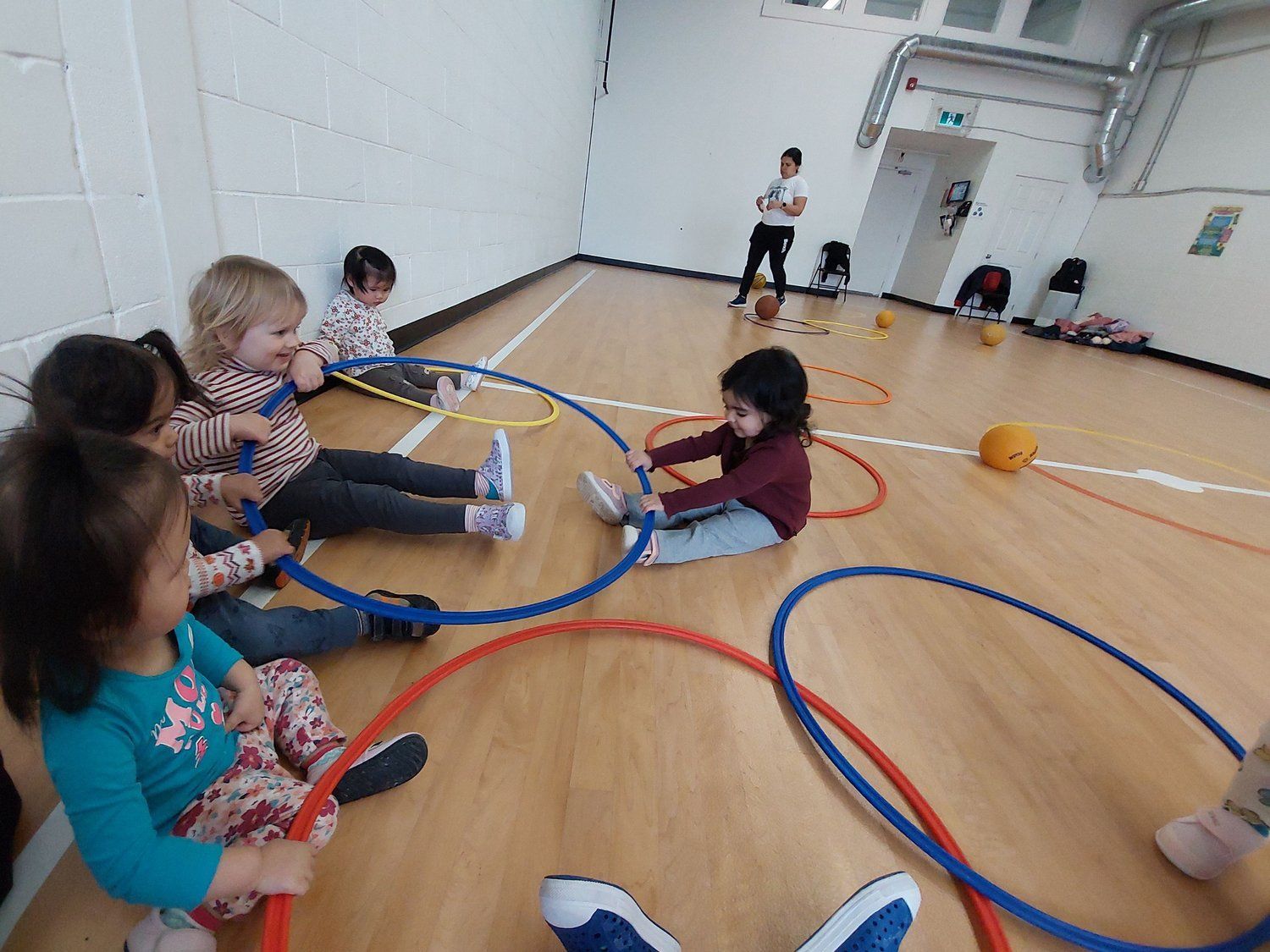 A group of children are sitting on the floor playing with hula hoops.