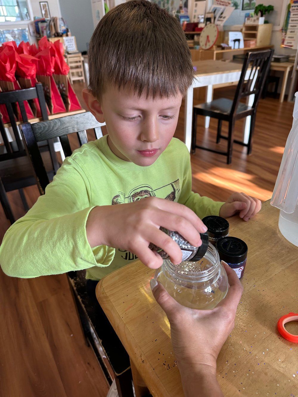 A young boy is sitting at a table making a snow globe.
