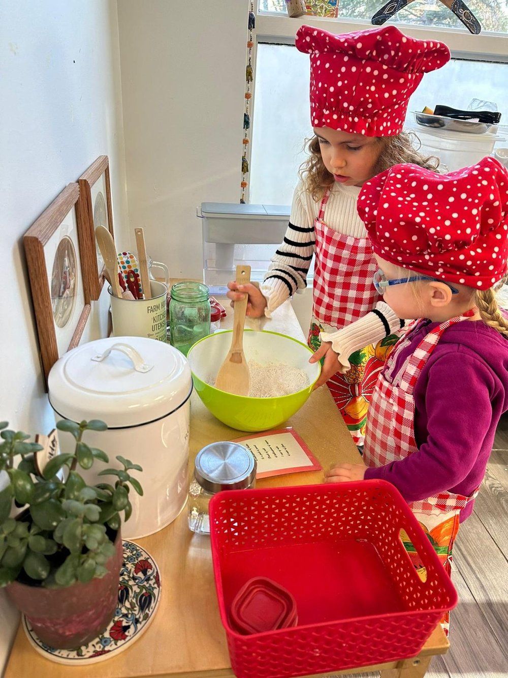 Two little girls are wearing chef hats and aprons and mixing ingredients in a bowl.