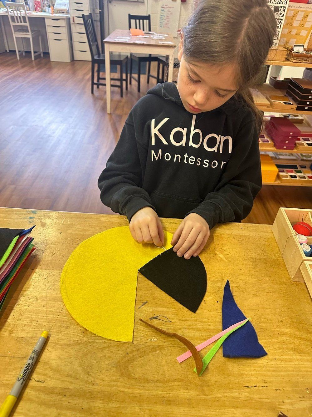 A little girl wearing a kaban sweatshirt is sitting at a table