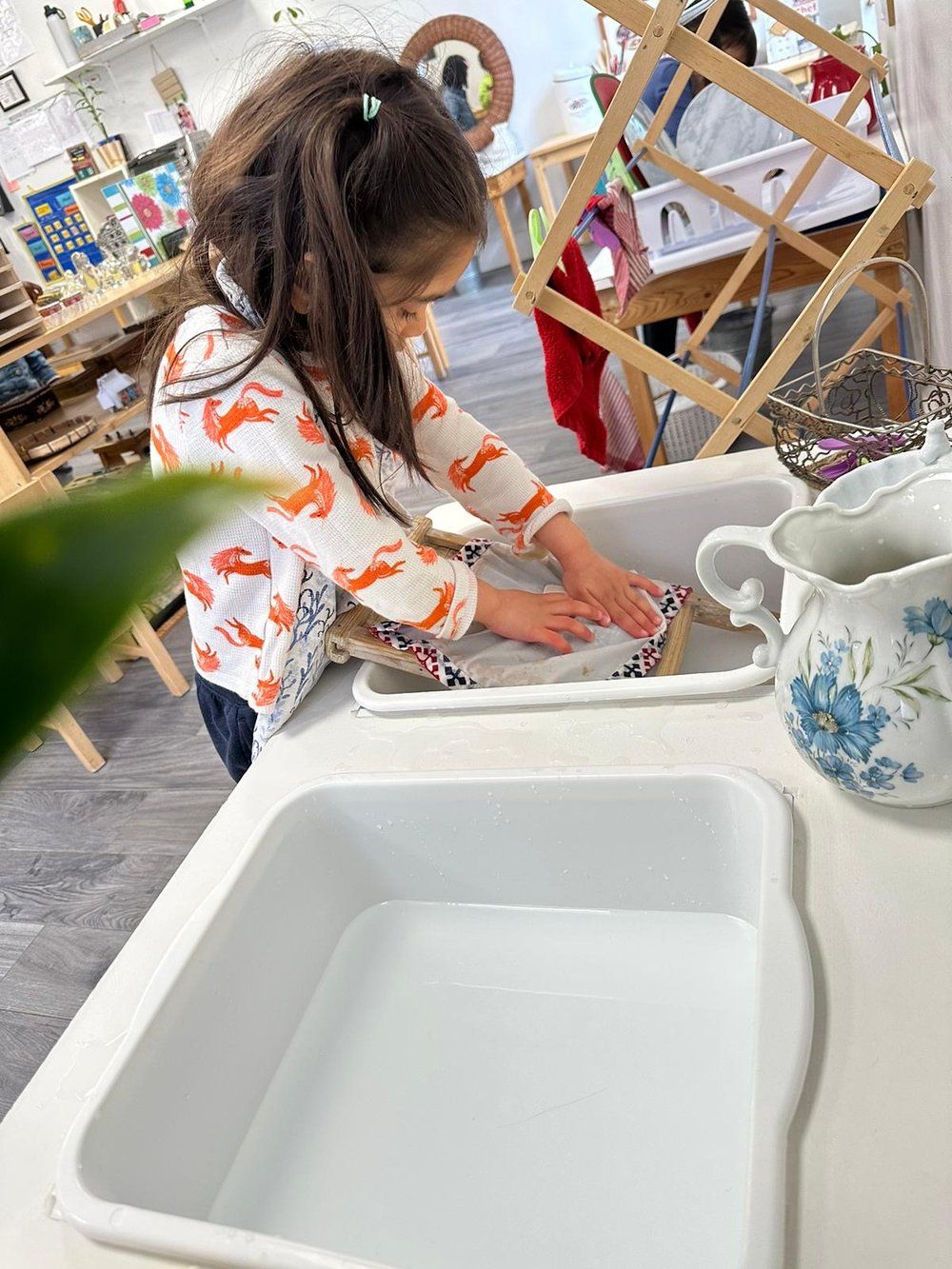 A little girl is washing dishes in a sink.