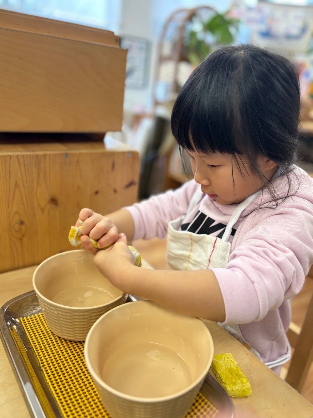 A little girl is playing with bowls on a table.