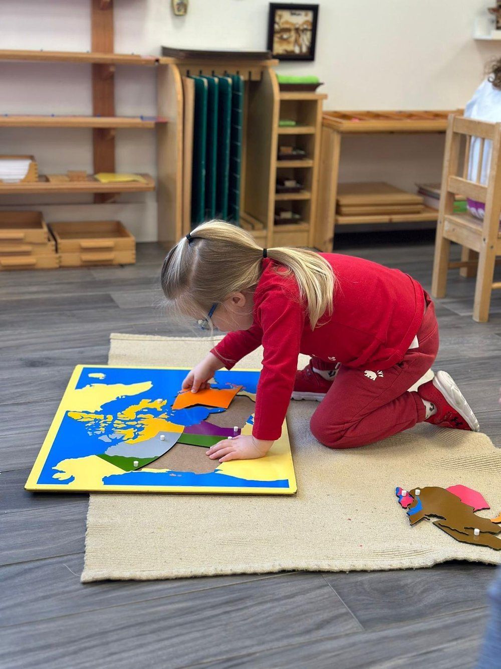 A little girl is kneeling on the floor playing with a puzzle.