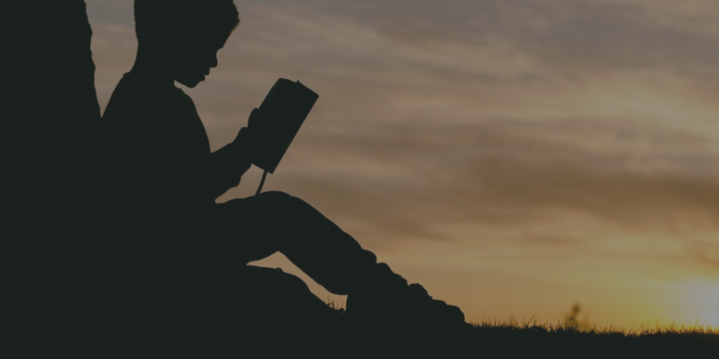 A silhouette of a montessori child reading a book at sunset.