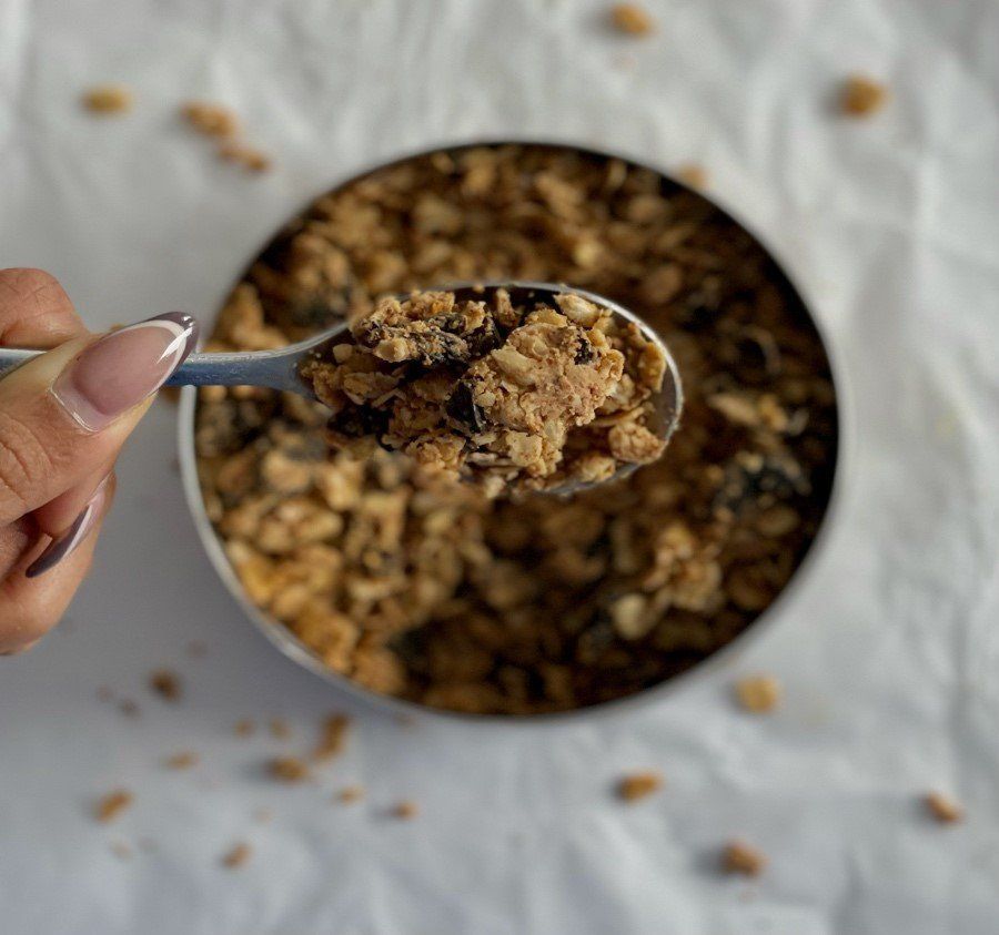 A person is holding a spoon in front of a bowl of granola.