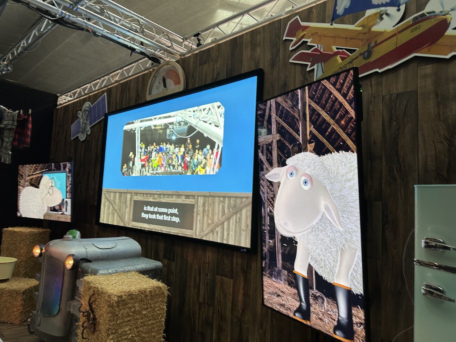 A sheep is standing in front of a screen in a room.