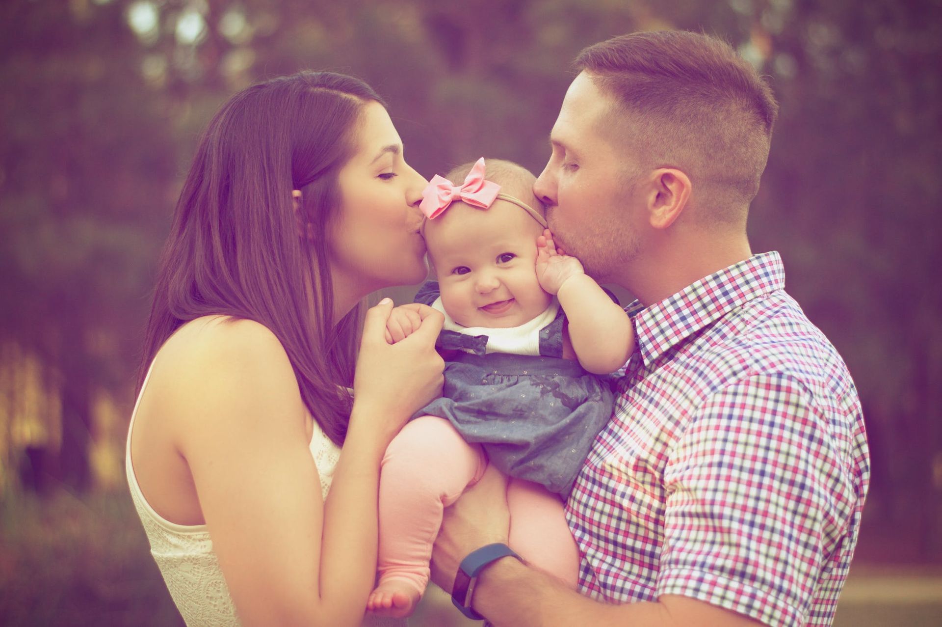 A man and a woman are kissing a baby on the cheek.