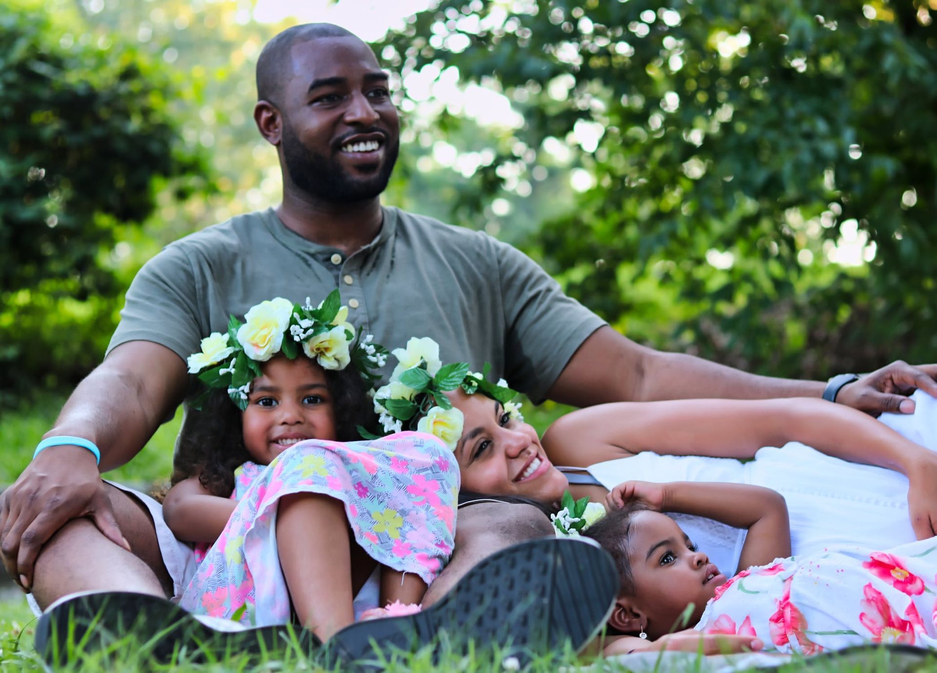 A man and woman are laying in the grass with two children wearing flower crowns.