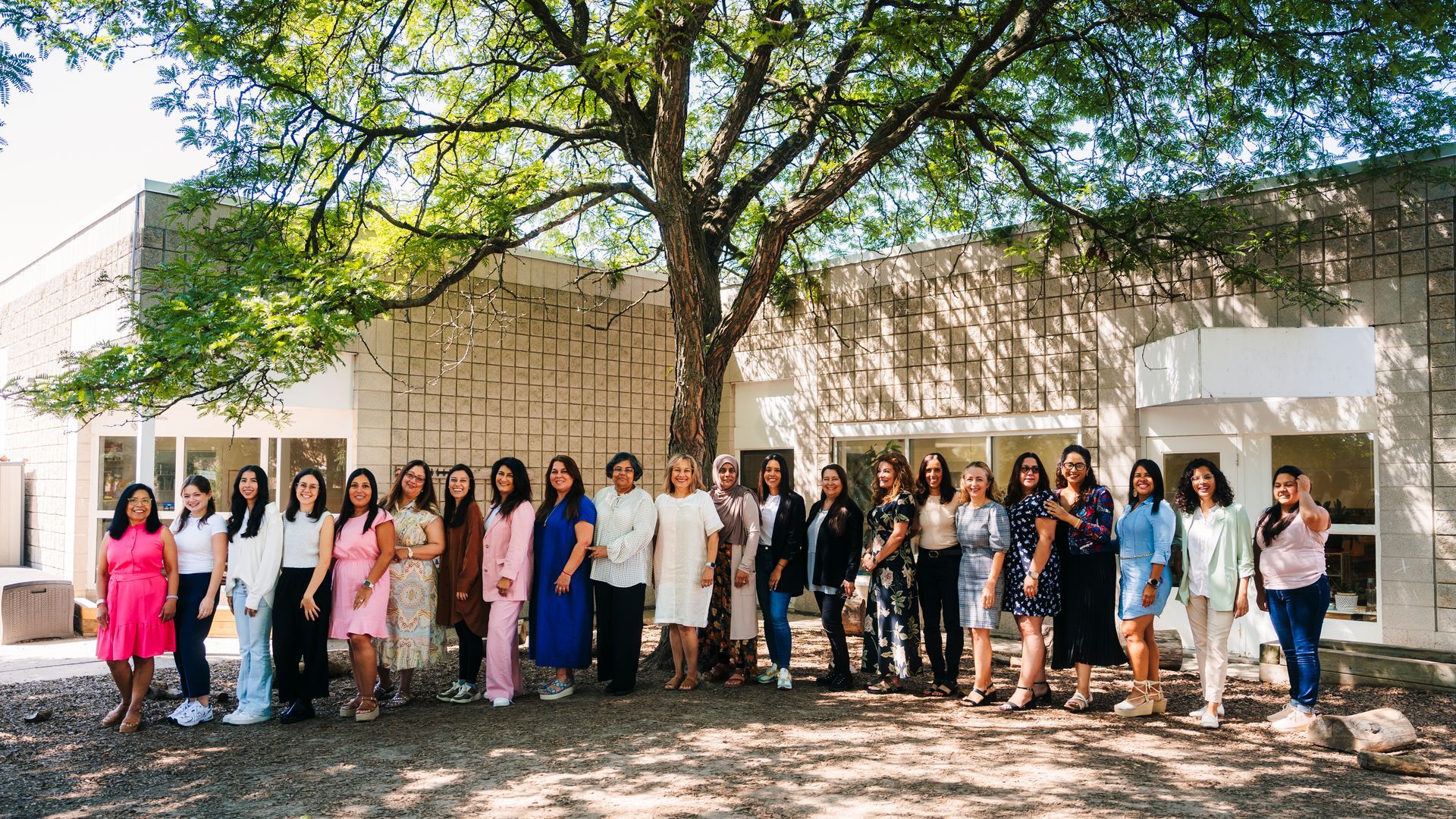 A group of women are standing in front of a building under a tree.