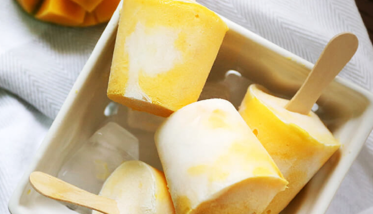 A white bowl filled with yellow and white ice pops with wooden sticks.