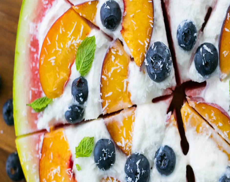 A watermelon pizza with peaches , blueberries and yogurt on a wooden table.