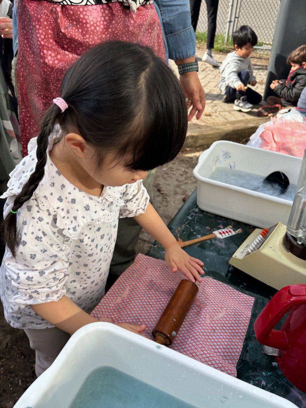 A little girl is playing with a rolling pin on a table.