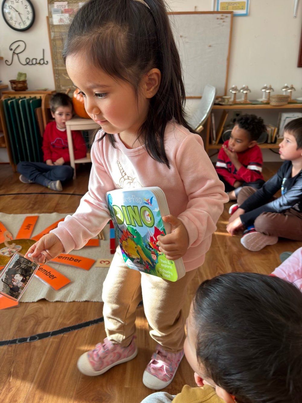 A little girl is reading a book to a group of children.