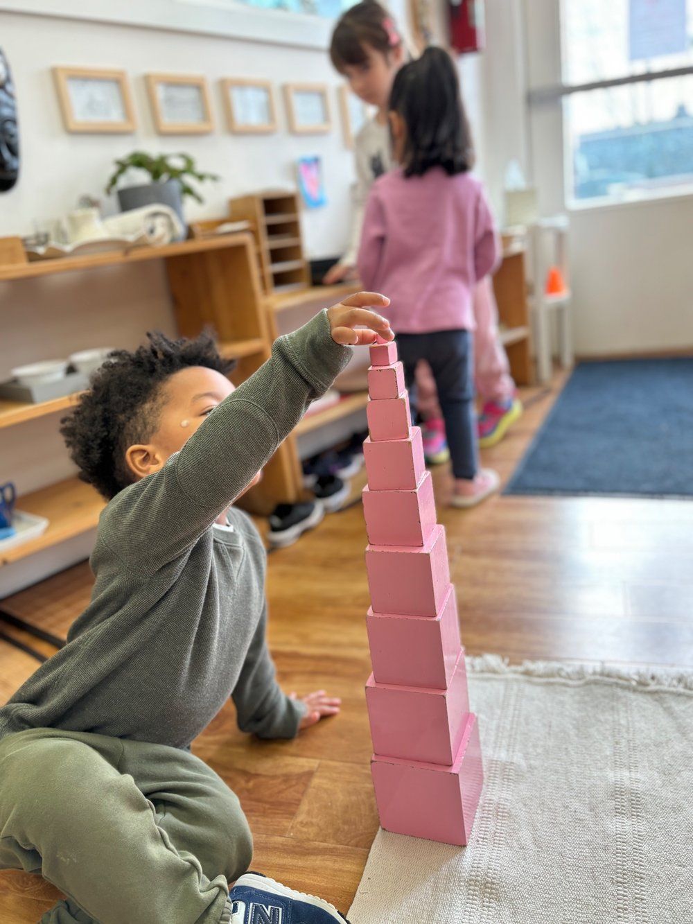 A young boy is sitting on the floor playing with pink blocks.