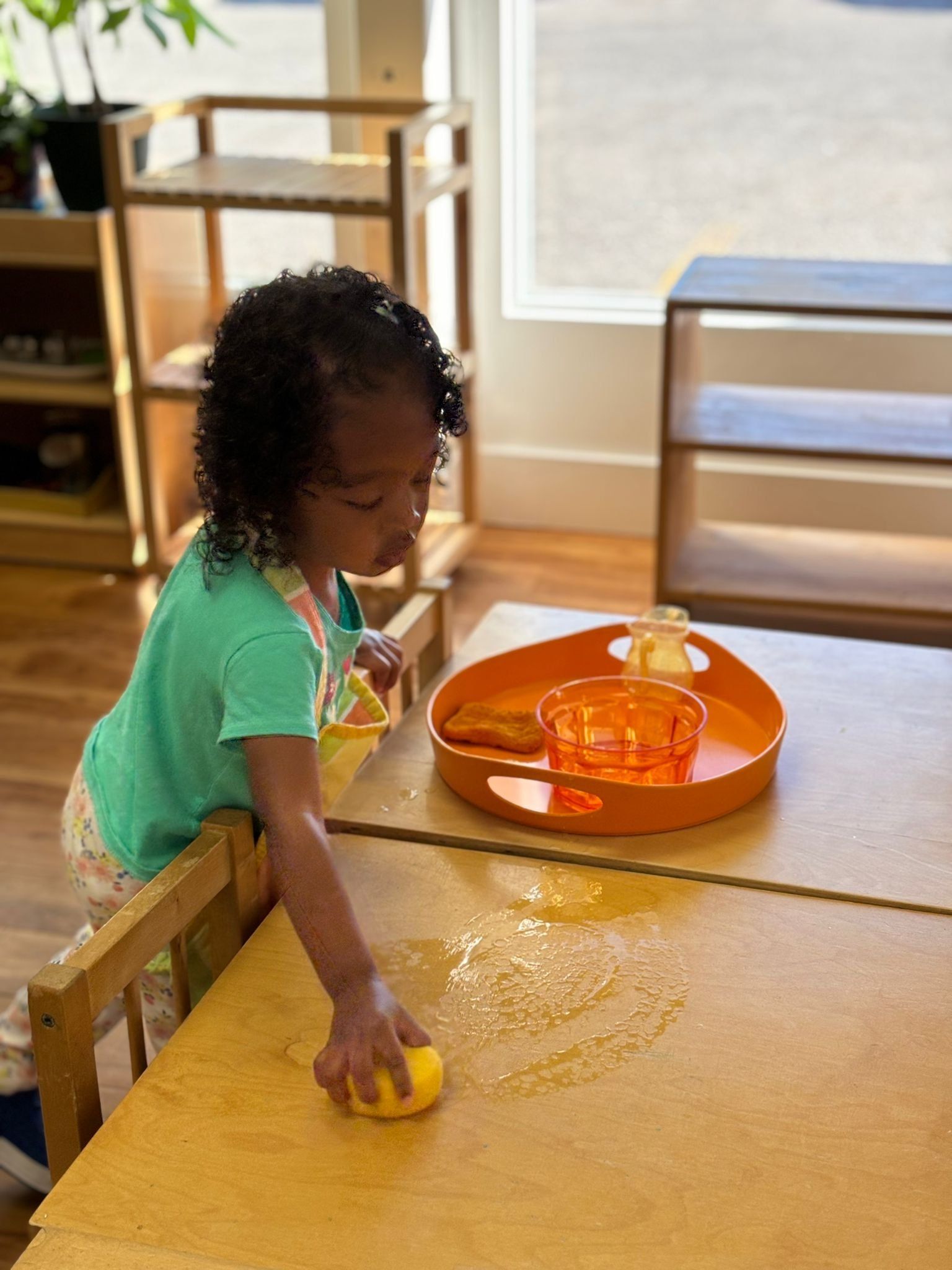 A little girl is playing with a yellow sponge on a table.