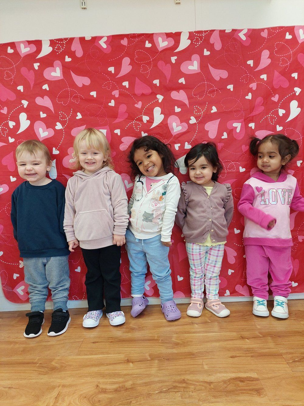 A group of children are standing in front of a wall with hearts on it.